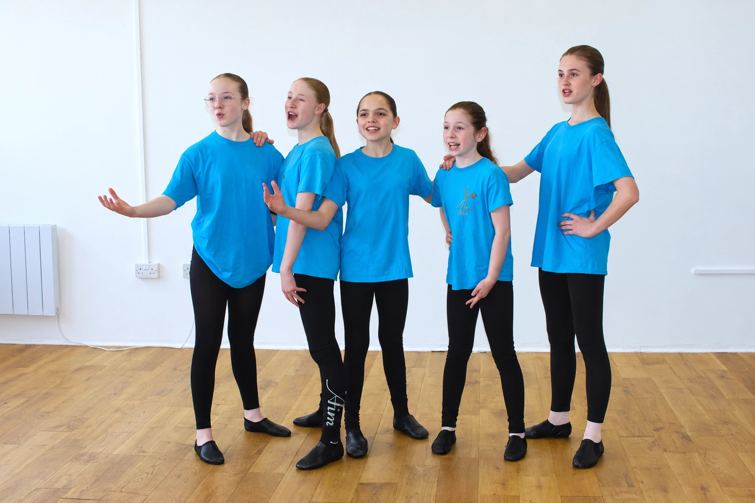 Students in turquoise AIM T-shirts singing together during a musical theatre lesson at Artists In Motion in Aylesham