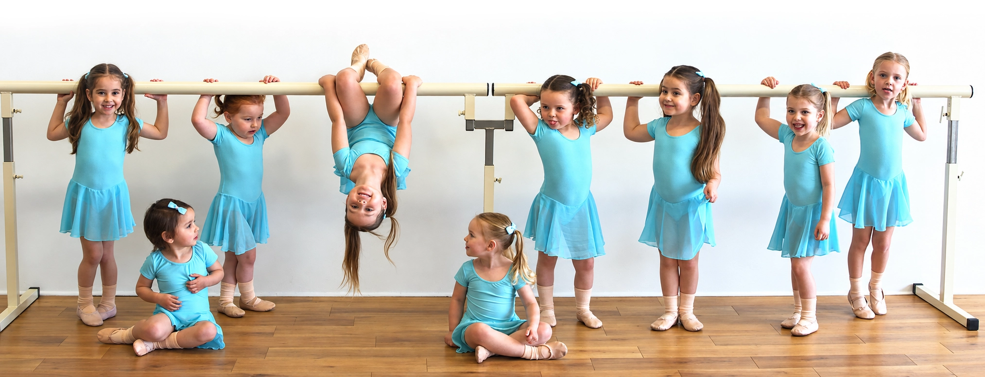 Young children in aqua dance outfits enjoying time together at a ballet barre